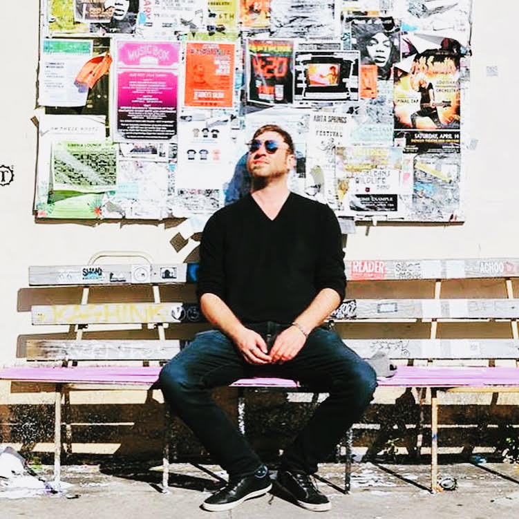 Tony, founder of Side B, sitting on a bench in front of a wall of concert posters.
